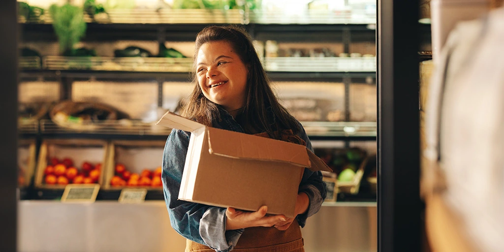 Autism independence demonstrated by a young woman carrying a cardboard box in a grocery store.