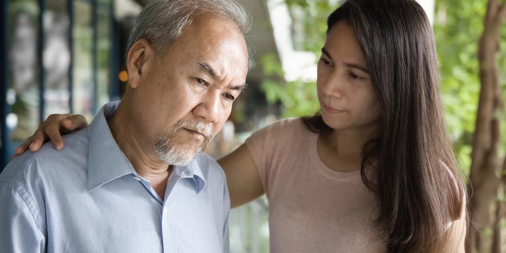 A concerned caregiver gently comforts an older man symbolizing the emotional support 