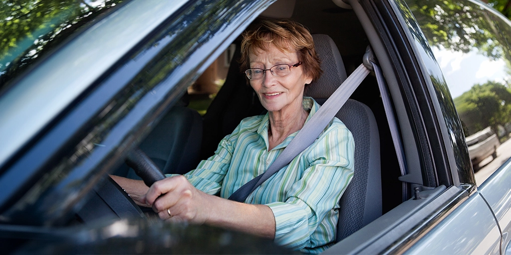 An elderly woman confidently drives a car, highlighting the importance of monitoring driving capabilities in dementia patients to ensure safety.