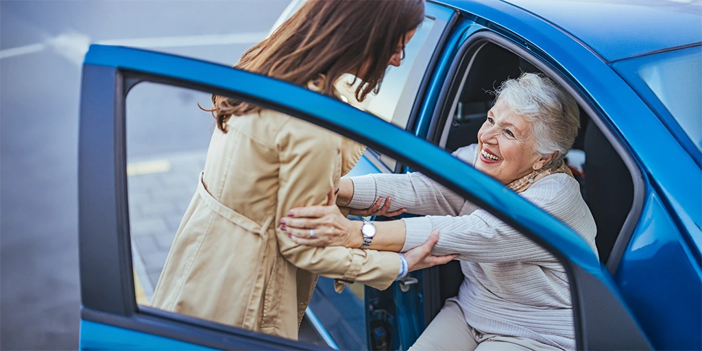 A caregiver assists an elderly woman out of a car
