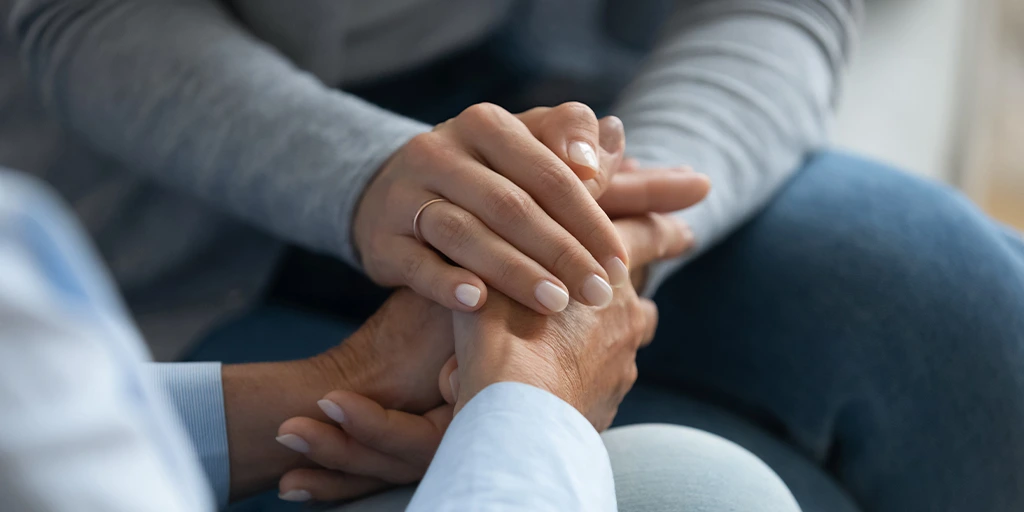 Close-up of a caregiver holding hands with an elderly person