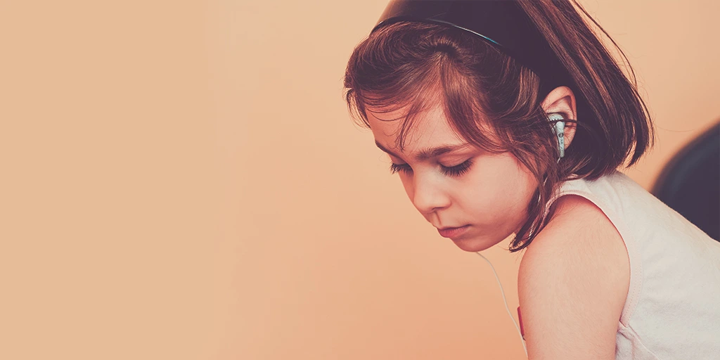 Young girl with autism wearing headphones, calmly focused, symbolizing early signs of sensory sensitivity.
